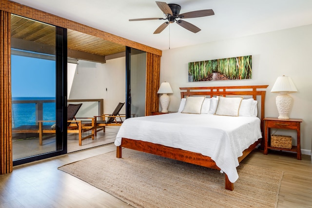 bedroom with a water view, wood-type flooring, and ceiling fan