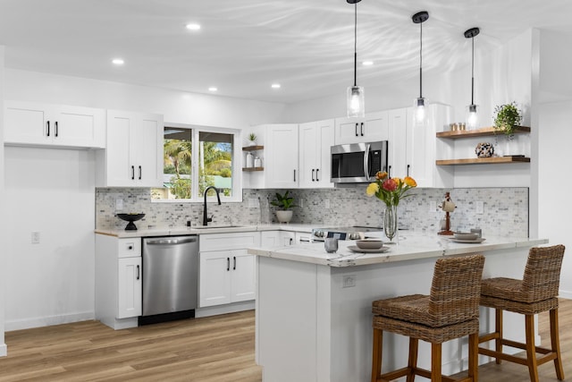 kitchen with light stone counters, stainless steel appliances, sink, decorative light fixtures, and white cabinets