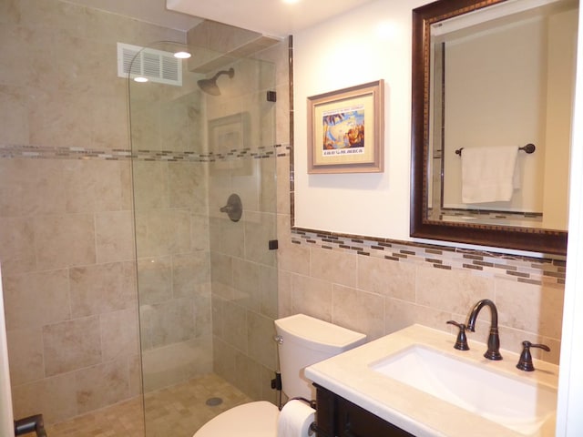 bathroom with vanity, toilet, tile walls, and tiled shower