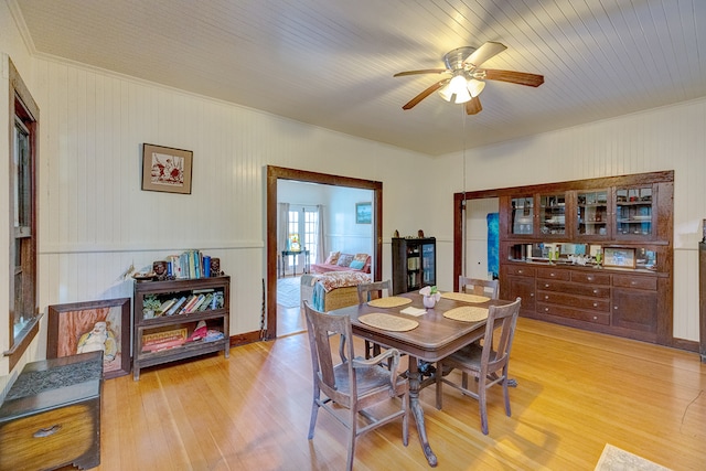 dining area featuring french doors, ornamental molding, ceiling fan, light wood-type flooring, and wood walls