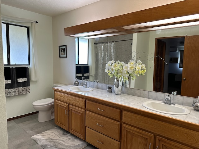 bathroom featuring baseboards, a sink, toilet, and double vanity