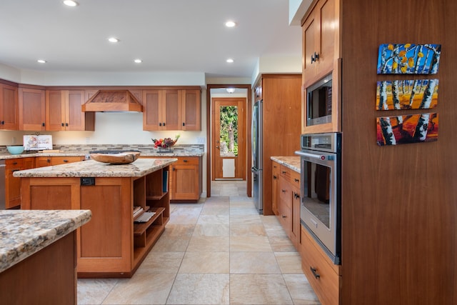 kitchen featuring stainless steel appliances, a center island, light stone counters, decorative backsplash, and wall chimney exhaust hood