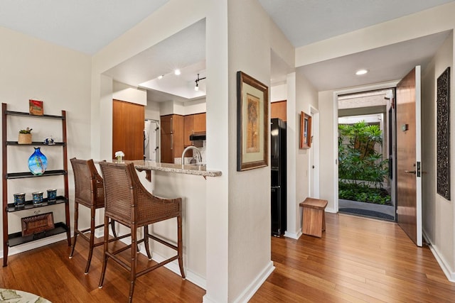 kitchen with black refrigerator, light stone countertops, hardwood / wood-style flooring, a breakfast bar, and kitchen peninsula