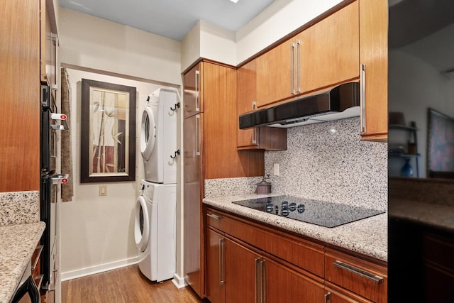 kitchen with stacked washer and clothes dryer, light stone counters, black electric stovetop, backsplash, and light hardwood / wood-style floors