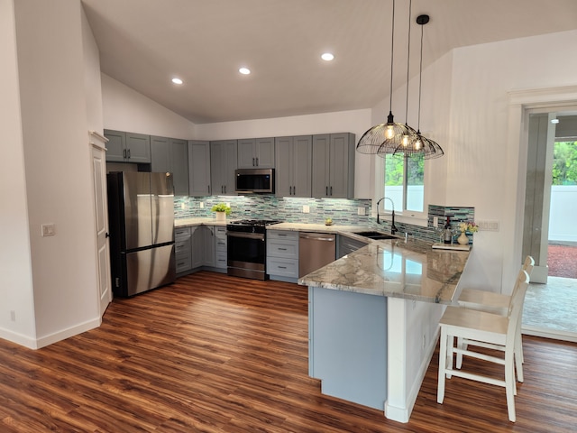 kitchen featuring kitchen peninsula, stainless steel appliances, dark wood-type flooring, sink, and hanging light fixtures