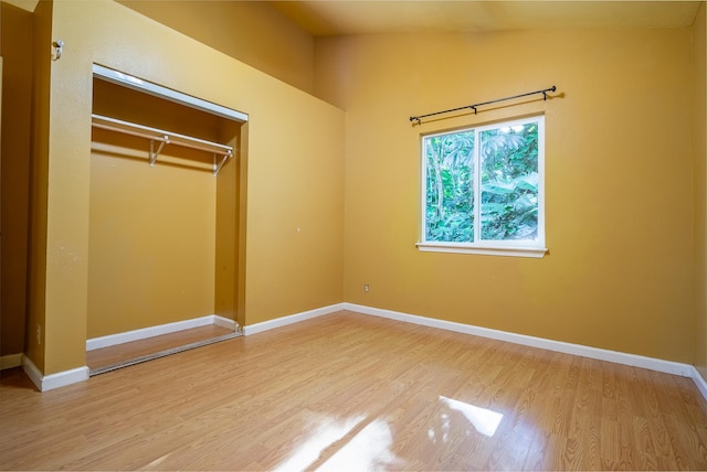 unfurnished bedroom featuring hardwood / wood-style floors, a closet, and lofted ceiling