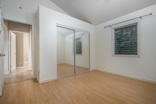 unfurnished bedroom featuring light hardwood / wood-style floors, lofted ceiling, and a closet