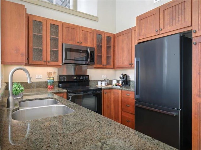 kitchen featuring black appliances, a sink, glass insert cabinets, and brown cabinets