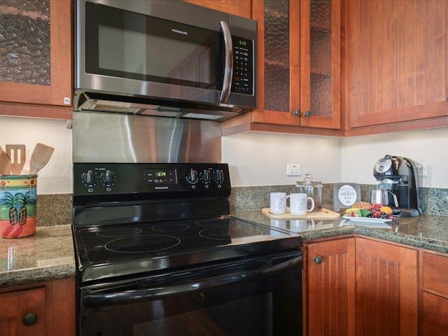 kitchen with electric range, stone countertops, glass insert cabinets, stainless steel microwave, and brown cabinets