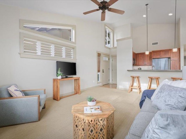 living area featuring light carpet, ceiling fan, visible vents, and a high ceiling