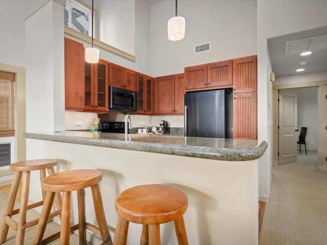 kitchen with stainless steel fridge, visible vents, glass insert cabinets, a breakfast bar area, and hanging light fixtures