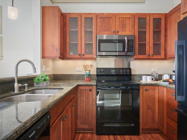 kitchen with stone counters, decorative light fixtures, glass insert cabinets, a sink, and black appliances