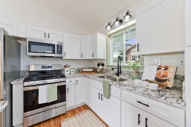 kitchen with stainless steel appliances, lofted ceiling, sink, and white cabinets