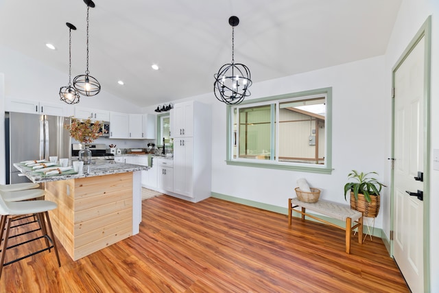 kitchen featuring white cabinets, appliances with stainless steel finishes, light stone countertops, vaulted ceiling, and light hardwood / wood-style flooring