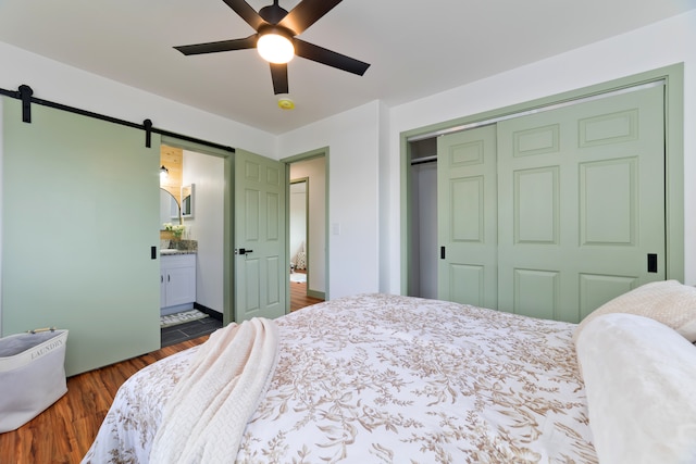 bedroom with a closet, ensuite bath, a barn door, dark hardwood / wood-style flooring, and ceiling fan