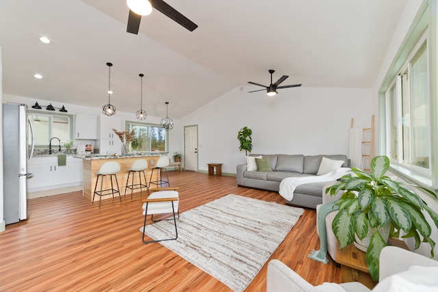 living room with light hardwood / wood-style floors, sink, ceiling fan with notable chandelier, and vaulted ceiling