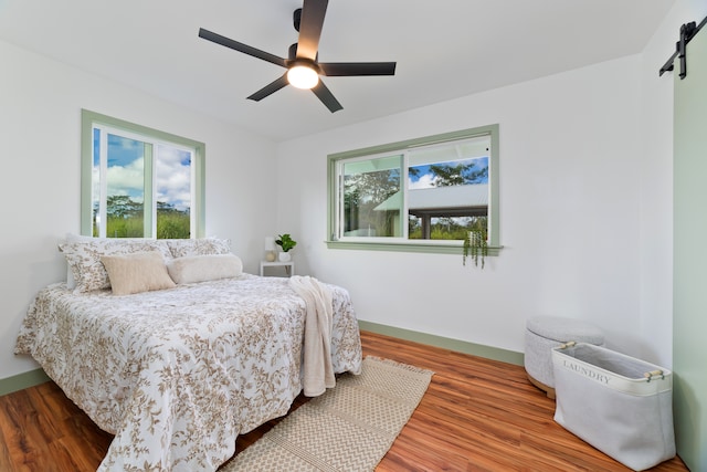 bedroom with a barn door, wood-type flooring, and ceiling fan