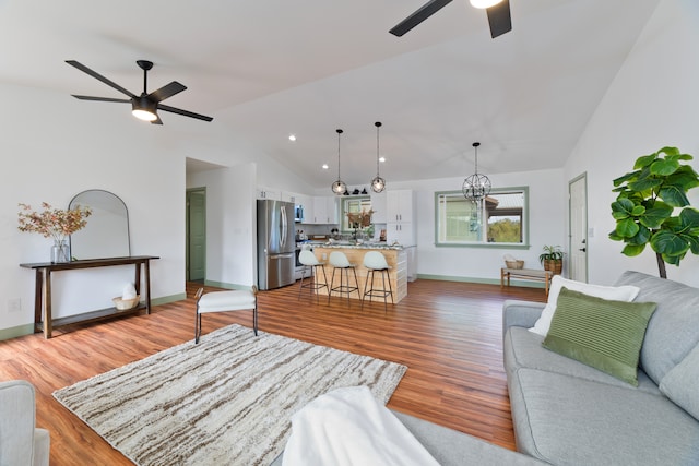 living room featuring lofted ceiling, wood-type flooring, and ceiling fan with notable chandelier