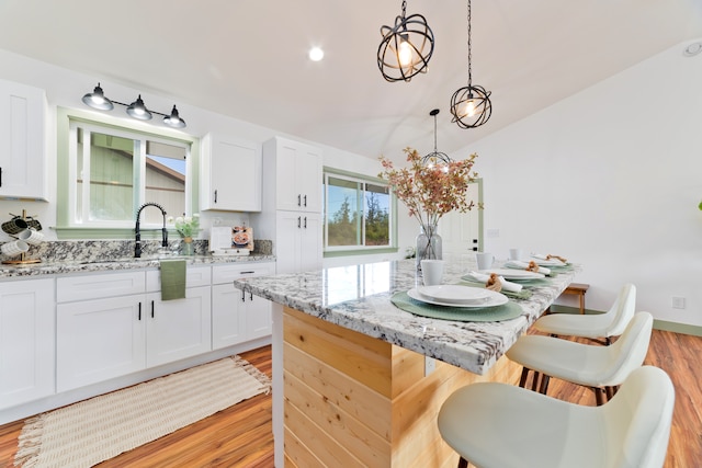 kitchen with light hardwood / wood-style flooring, white cabinetry, light stone countertops, and hanging light fixtures