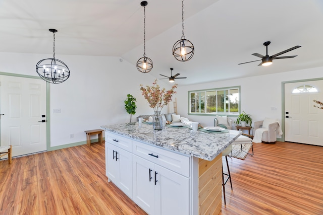 kitchen with light wood-type flooring, a kitchen island, decorative light fixtures, vaulted ceiling, and white cabinets