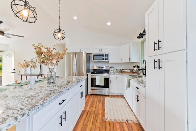 kitchen with stainless steel appliances, lofted ceiling, pendant lighting, white cabinets, and light hardwood / wood-style flooring