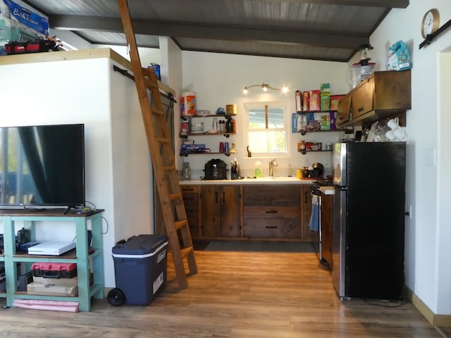 kitchen with light wood-type flooring, dark brown cabinetry, vaulted ceiling with beams, and black fridge