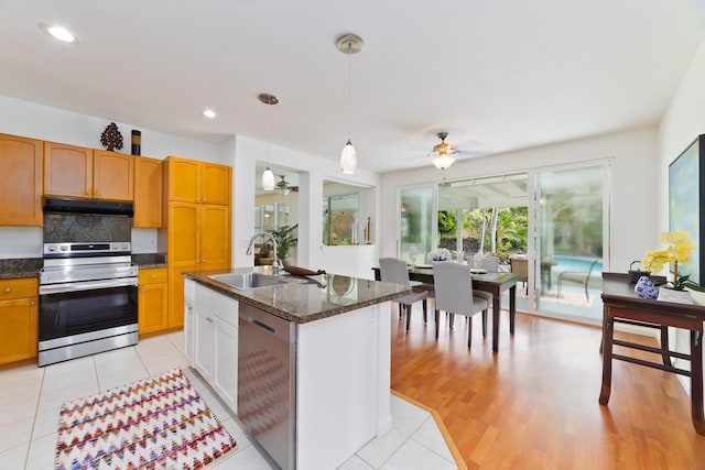 kitchen with stainless steel appliances, ceiling fan, sink, pendant lighting, and a center island with sink