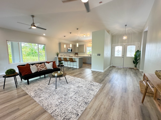 living room with light hardwood / wood-style floors, french doors, ceiling fan with notable chandelier, and vaulted ceiling