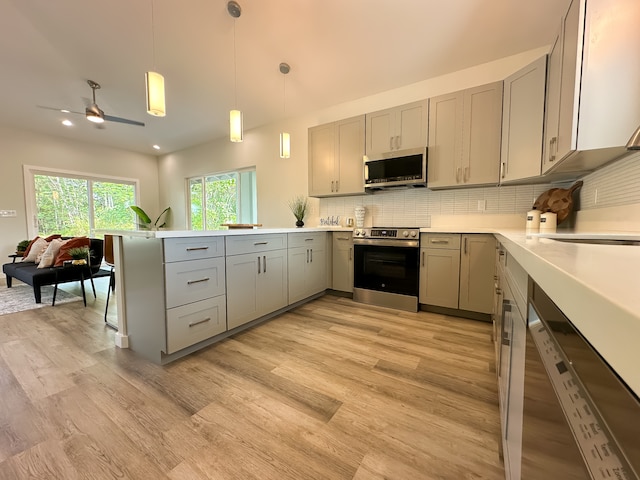 kitchen with kitchen peninsula, hanging light fixtures, backsplash, gray cabinetry, and stainless steel appliances