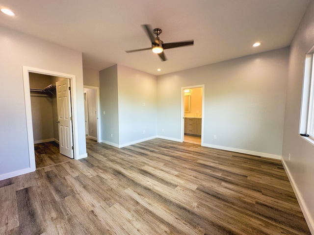 unfurnished bedroom with a closet, a walk in closet, dark hardwood / wood-style flooring, ensuite bathroom, and ceiling fan