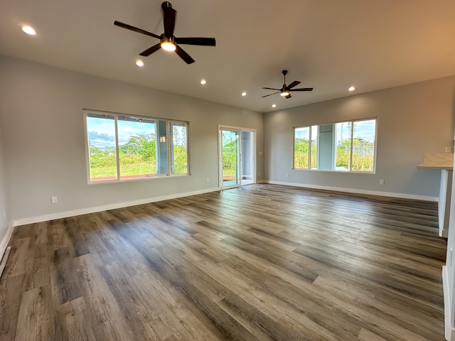 unfurnished living room featuring a wealth of natural light, dark wood-type flooring, and ceiling fan