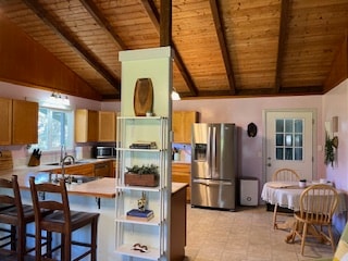 kitchen featuring stainless steel appliances, a breakfast bar area, wood ceiling, and vaulted ceiling with beams