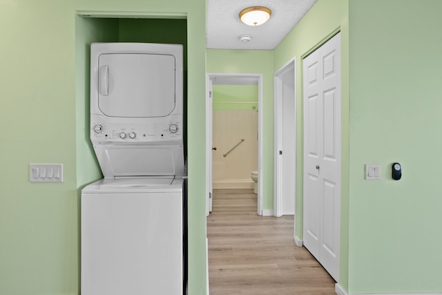 laundry area featuring light hardwood / wood-style flooring, a textured ceiling, and stacked washer and clothes dryer