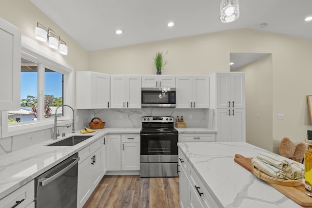 kitchen with light stone countertops, sink, hardwood / wood-style floors, stainless steel appliances, and lofted ceiling