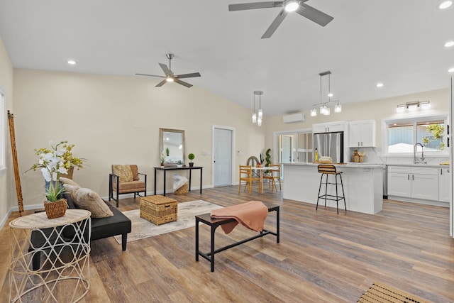 living room with ceiling fan, vaulted ceiling, and light wood-type flooring