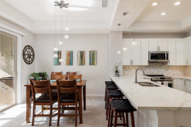 kitchen featuring kitchen peninsula, light stone counters, appliances with stainless steel finishes, white cabinetry, and sink