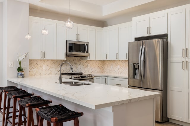 kitchen featuring kitchen peninsula, hanging light fixtures, a breakfast bar, white cabinetry, and stainless steel appliances