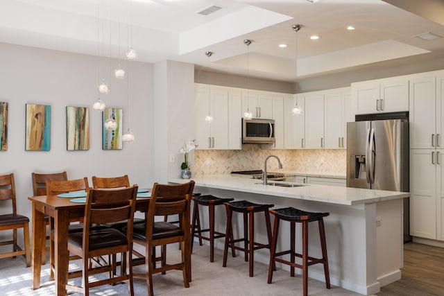 kitchen featuring pendant lighting, white cabinets, stainless steel appliances, and a tray ceiling