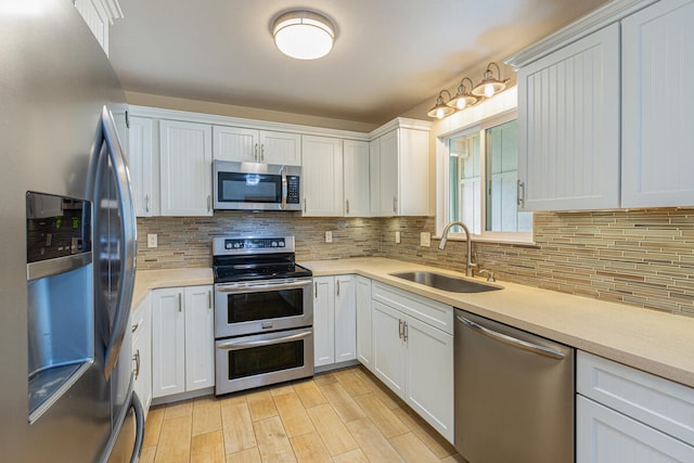 kitchen featuring sink, light wood-type flooring, tasteful backsplash, white cabinetry, and stainless steel appliances