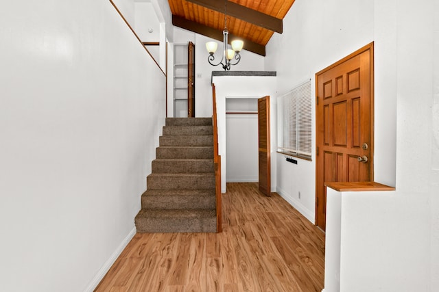 staircase featuring hardwood / wood-style flooring, beam ceiling, wooden ceiling, a chandelier, and high vaulted ceiling