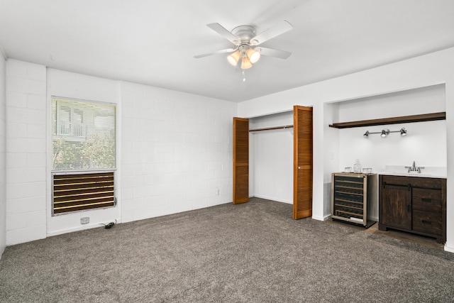 unfurnished bedroom with wine cooler, ceiling fan, dark colored carpet, a closet, and sink