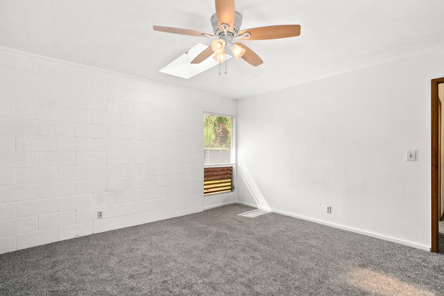 spare room with ceiling fan, a skylight, and dark colored carpet