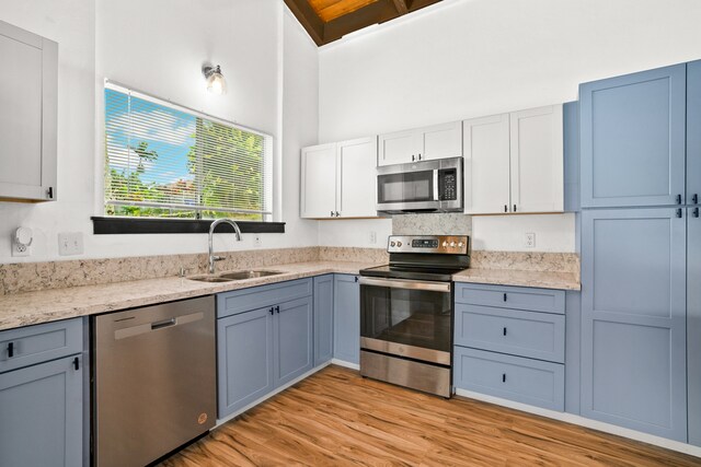 kitchen with stainless steel appliances, sink, light wood-type flooring, white cabinetry, and light stone counters