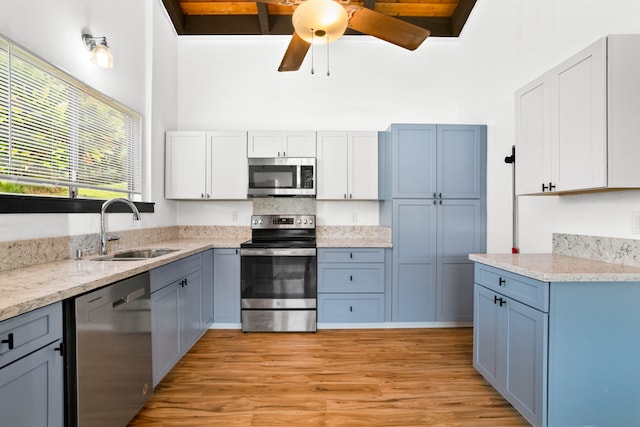 kitchen with appliances with stainless steel finishes, sink, white cabinetry, light hardwood / wood-style floors, and beamed ceiling