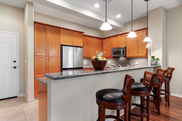 kitchen featuring kitchen peninsula, tasteful backsplash, hanging light fixtures, dark stone counters, and stainless steel appliances