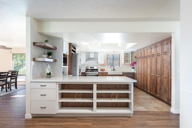 kitchen featuring sink, white cabinets, kitchen peninsula, stainless steel appliances, and wall chimney exhaust hood