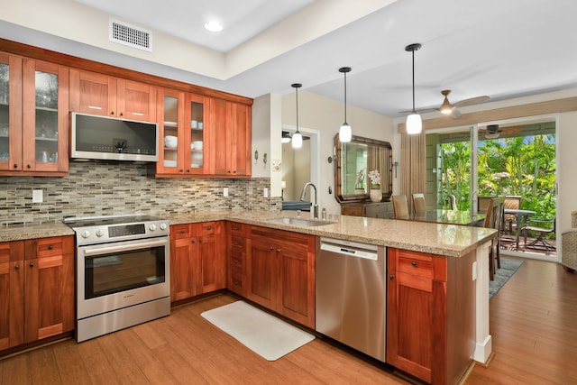 kitchen featuring appliances with stainless steel finishes, kitchen peninsula, light stone countertops, and light wood-type flooring