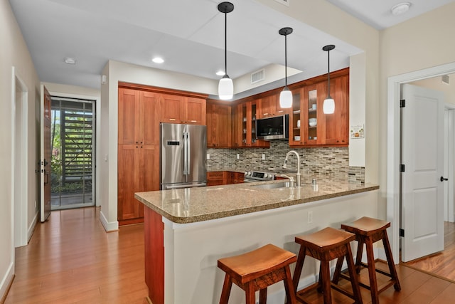 kitchen featuring kitchen peninsula, light stone counters, appliances with stainless steel finishes, light hardwood / wood-style floors, and decorative light fixtures