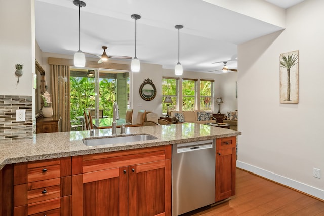 kitchen featuring light stone counters, stainless steel dishwasher, a sink, open floor plan, and light wood-type flooring