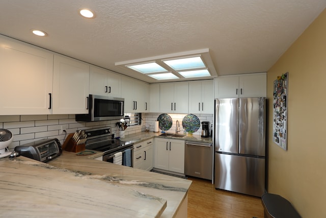 kitchen featuring decorative backsplash, stainless steel appliances, sink, light wood-type flooring, and white cabinets